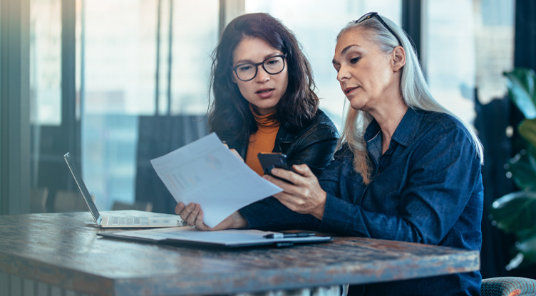 Two women working at a desk looking at phone