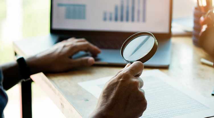 man using magnifying glass to look at investment charts