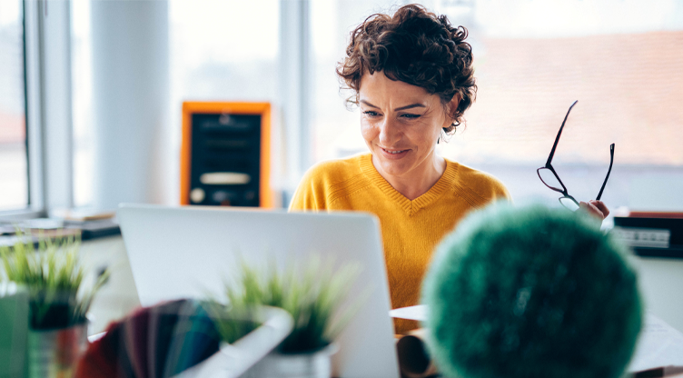 woman taking off her glasses and looking at laptop